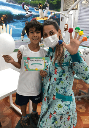 Dra. Isabelle abraçada com paciente criança sorrindo para a foto durante atendimento odontológico